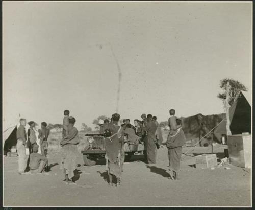 Group of people standing with John Marshall, and a person in the expedition Jeep (print is a cropped image)