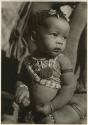 Baby wearing beads, full-length portrait (print is a cropped image)