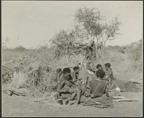 Group of women sitting, one of them wiping off a child who has defecated (print is a cropped image)