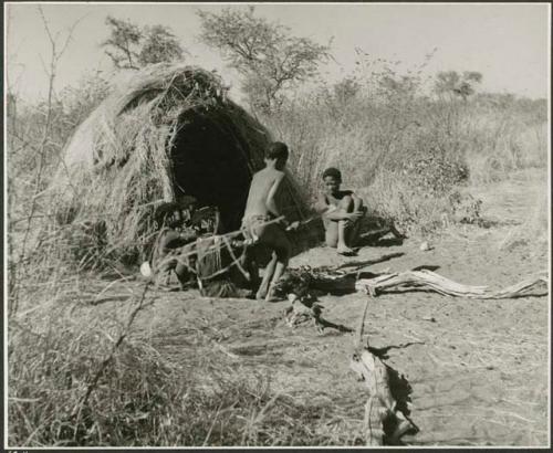 "Little N!ai" and /Gunda (son of Khwan//a and her former husband) sitting by their skerm with their wedding party, including Tsamgao (son of ≠Toma and !U), ≠Gisa (daughter of ≠Gao and Khwo//o-/Gasa), Xama (daughter of "Gao Helmet" and //Kushay), ≠Gao (son of Gau and Be), and a boy playing the //guashi (print is a cropped image)