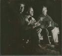 Lorna Marshall, John Marshall, and Laurence Marshall sitting by a fire (print is a cropped image)