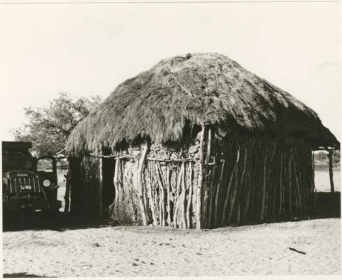 Okwa hut with a vehicle beside it (print is a cropped image)