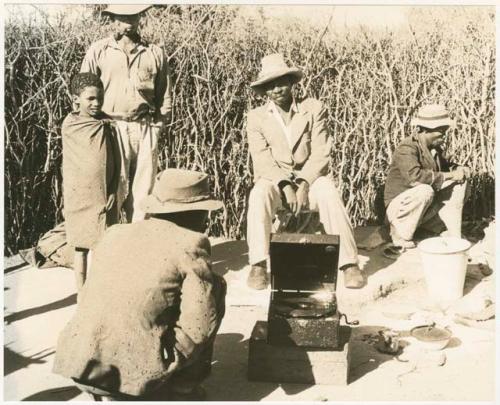 Boys, Chuana, and four other people listening to Boys' phonograph (print is a cropped image)