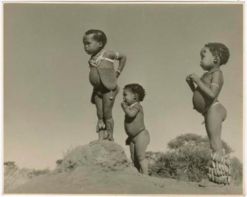 /Gaishay (son of "Gao Medicine" and Di!ai), Bau (daughter of "Crooked /Qui"), and "Little ≠Gao" (son of "/Qui Navel") standing on an ant hill (print is a cropped image)