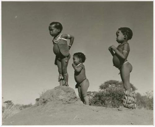 /Gaishay (son of "Gao Medicine" and Di!ai), Bau (daughter of "Crooked /Qui"), and "Little ≠Gao" (son of "/Qui Navel") standing on an ant hill (print is a cropped image)