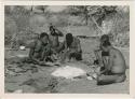 Group of men sitting and working around a heap of ashes, including "Old Gau" (Band 1), ≠Gao (husband of Khwo//o-/Gasa, and brother of "Old Gau," /Gaishay, unidentified man, and "/Qui Navel" (print is a cropped image)