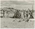 Two people standing out in front of a hut (print is a cropped image)