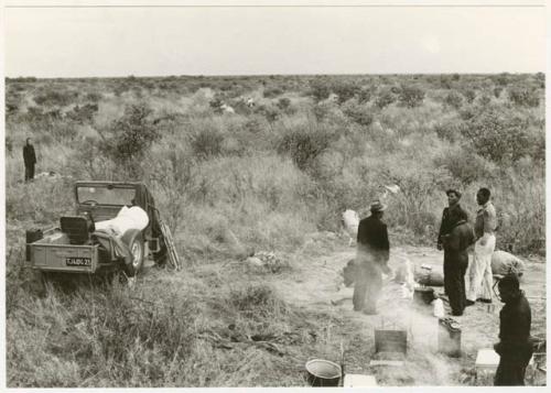 Five people standing in the camp with Elizabeth Marshall Thomas standing in the distance (print is a cropped image)