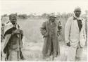 Boy in a suit, a man in an overcoat and hat, standing beside two other men (print is a cropped image)