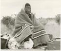 Dabe wrapped in a blanket sitting on top of a truck (print is a cropped image)