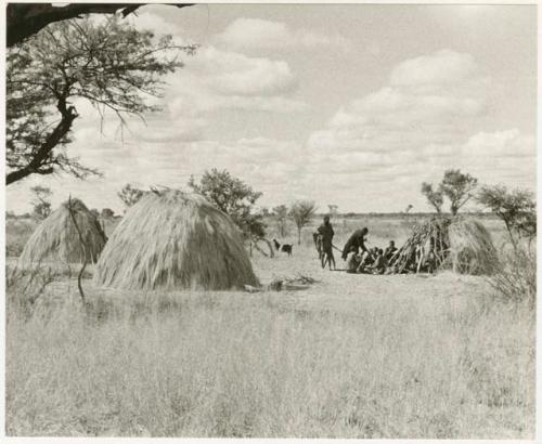 Group sitting between two huts (print is a cropped image)