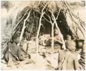 Group sitting in front of a grass hut at Kungwane (print is a cropped image)