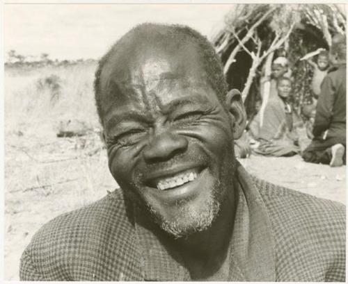 Man in a checked coat smiling (print is a cropped image)