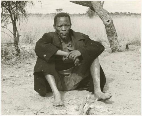 Man in a black overcoat sitting (print is a cropped image)