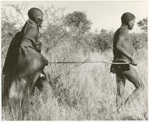 Elderly blind man led by a boy using a long stick (print is a cropped image)