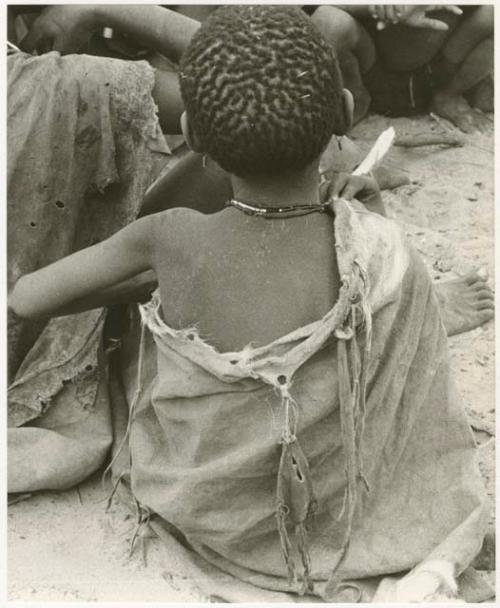 Rear view of a child sitting in a group (print is a cropped image)