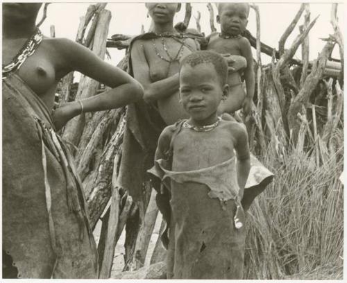 Child standing with three women in the background (print is a cropped image)