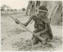 Woman on her knees digging with a hoe (print is a cropped image)