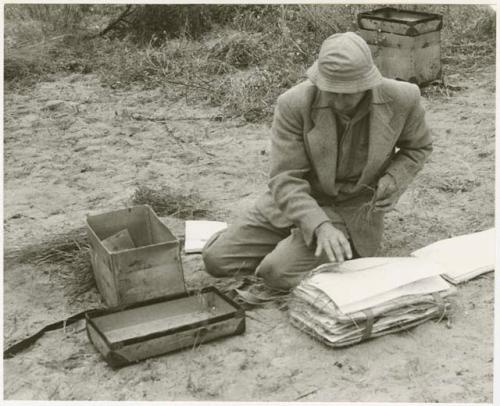 Robert Story sitting on the ground, packing specimens (print is a cropped image)