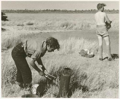 Two expedition members, one changing clothes, one getting water (print is a cropped image)