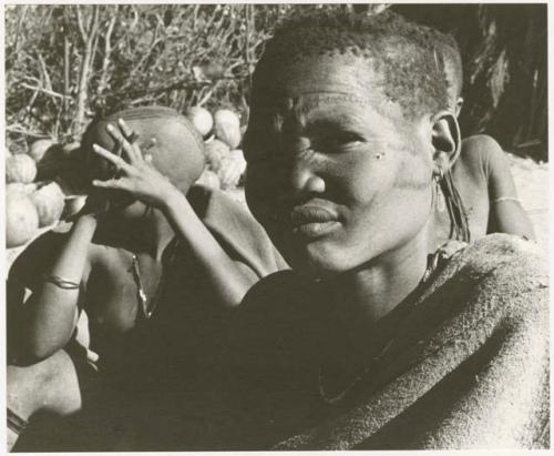 Woman sitting, close- up portrait; three others in the background (print is a cropped image)