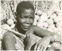 Woman sitting holding a long stick in her hands; tsama melons in the background (print is a cropped image)