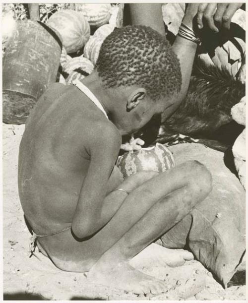 Boy sitting eating a tsama melon (print is a cropped image)