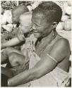 Elderly woman and two children sitting in a row; tsama melons in the background (print is a cropped image)