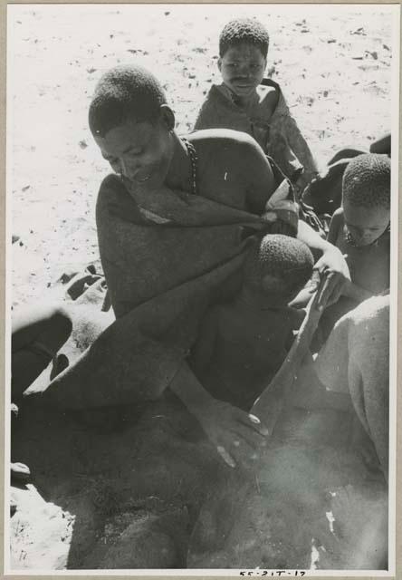 Woman sitting with three children, digging with a fire paddle