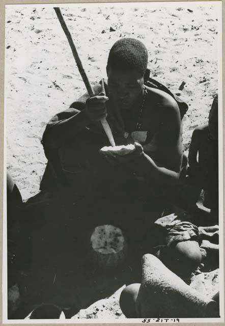 Woman seating with a digging stick, eating a tsama melon