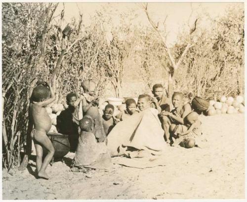 Group sitting by a pile of tsama melons (print is a cropped image)