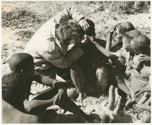 Elizabeth Marshall Thomas putting ointment in Oukwane's eyes; the group watching (print is a cropped image)