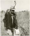 Man wearing a feather in his hat, walking (print is a cropped image)