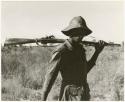 Headman carrying a gun over his shoulder, view from behind (print is a cropped image)