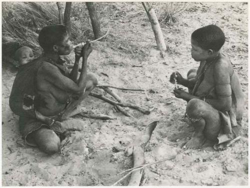 Rukan and Genitsu, with a baby on her back, sitting and lighting their pipes (print is a cropped image)