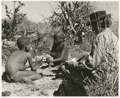 /Gaiamakwe and !Ou/ke playing a hand game; Lorna Marshall taking notes (print is a cropped image)