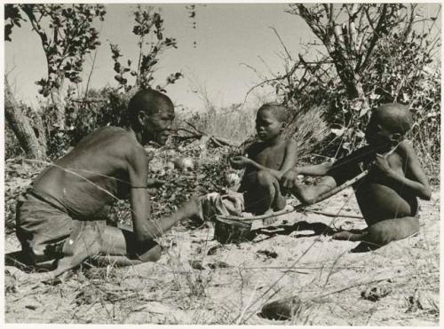 Twikwe, /Gaiamakwe, and !Ou/ke sitting playing musical bow (print is a cropped image)