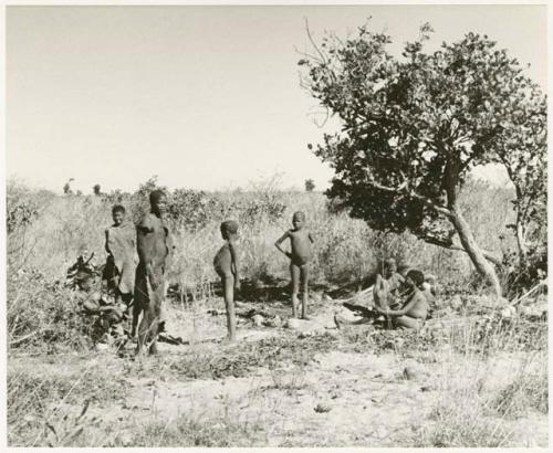 Group of people sitting and standing next to a tree (print is a cropped image)