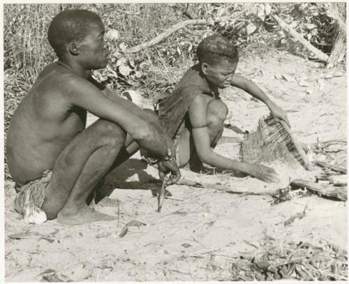 Tsekue sifting roasted tsama melon seeds from ashes, !Gai sitting beside her (print is a cropped image)