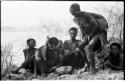 Group of Ju/'hoansi sitting; one woman is half crouching