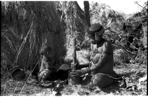 //Kushay ("Gao Helmet's" second wife) pounding with mortar and pestle while her child watches