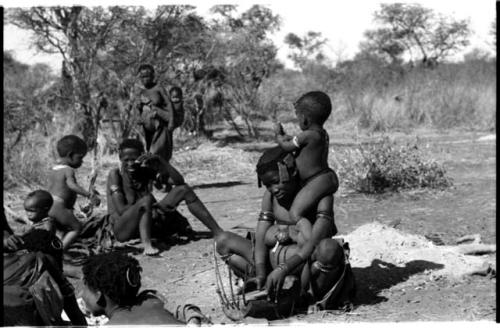 Group of Ju/'hoansi seated including Khuan//a (Gau's second wife) and //Kushay ("Gao Helmet's" second wife) sitting and playing the //guashi with her child seated on her shoulder