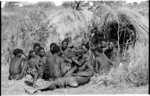 Group of Ju/'hoansi telling stories including left to right: "Lame ≠Gao" seen from behind, ≠Gao (Khwo//o-/Gasa's husband), "Gao Medicine," unidentified person seen from behind, ≠Toma, !Naishi, "Old Xama" with her hands over her head, "Gao Helmet" in profile, "Old Demi" lying down, "Crooked /Qui," Gao (Debe's son, Zuma's husband), ≠Toma (!Naishi's son), and Zuma (Gao's wife)