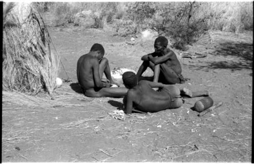 "/Qui Navel" making arrows by a fire and an unidentified person and "Old Gau" sitting to the right, watching him