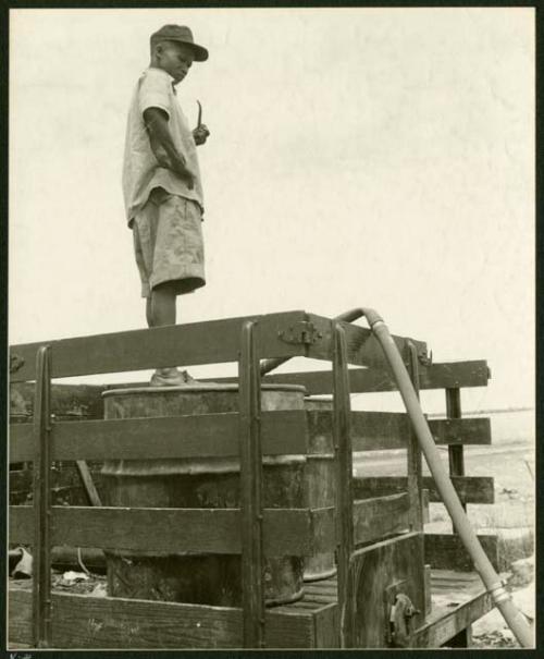 Man standing in the bed of a truck on a barrel watching as water is pumped into the barrel