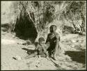 Khuan//a (Gau's wife) and her son, /Qui, sitting by a skerm; /Qui is playing with a musical bow