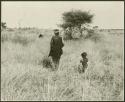 Woman and child, seen from the back; another person crouching in a tsĩ field in the background