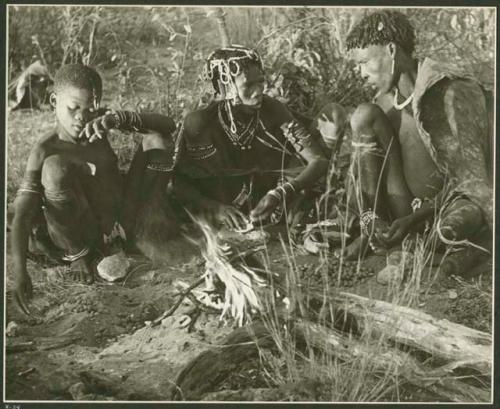 Husband, wife, and her younger sister sitting around a fire, roasting tsĩ