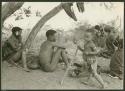 Group of Ju/'hoansi sitting in a werft; Left to right: /Gasa (/Qui's wife and !Naishi's daughter), /Qui (Gao's brother), //Kushay (/Gasa and /Qui's daughter) holding a stick, and other unidentified people