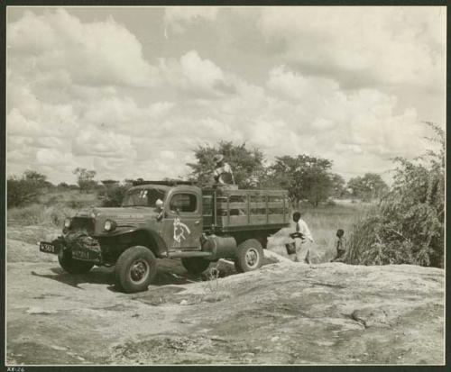 Power Wagon at a waterhole; three people filling barrels with buckets of water